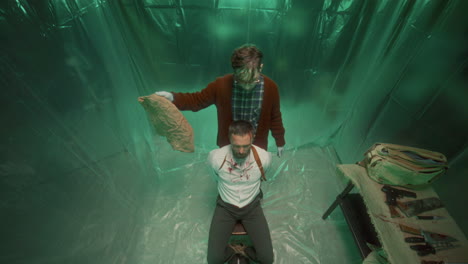 view from above of gloved psycho killer removing sack from head of hostage