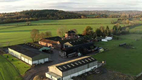 drone aerial footage of rural farm, farm buildings and barns, agriculture in the english countryside at morning, sunrise