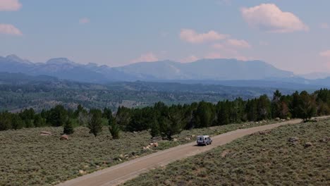 aerial rearview orbit follows camper truck driving on dirt road in wyoming’s wind river range, showcasing wide plains and mountains