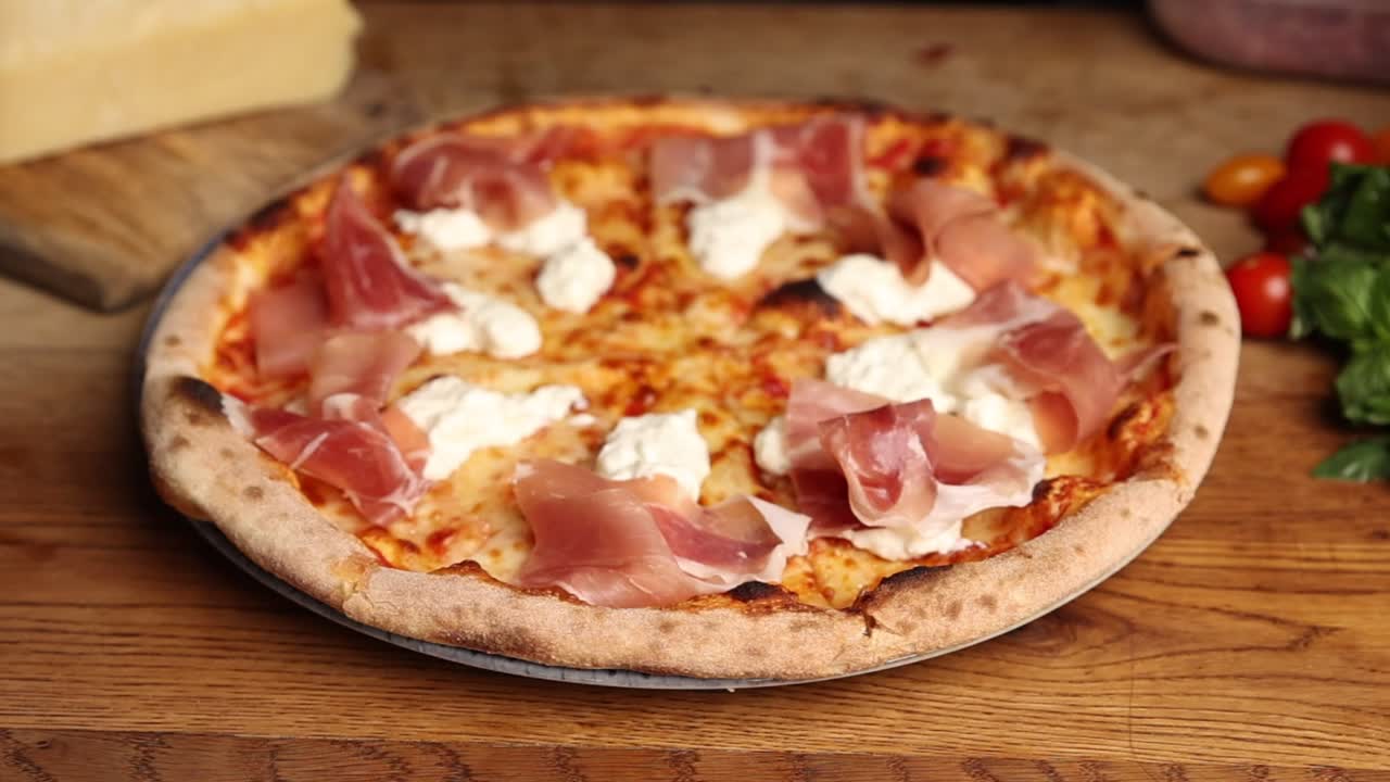 Mani dello chef che aggiungono formaggio fresco a una pizza al prosciutto