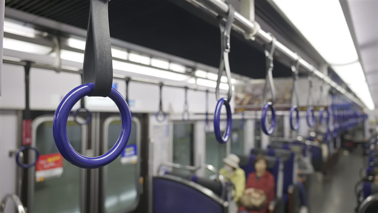Inside a public transport train, blue hand grips hang from the ceiling, providing support for passengers. Kyoto, Japan