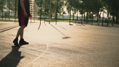 skillfull male basketball player dribbling ball against opposing defender, while playing streetball game at urban court at sunset