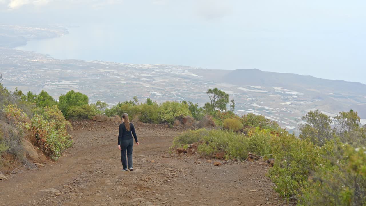A rallentatore, un turista che scende un ripido sentiero, guardando sulla panoramica Valle di Guimar