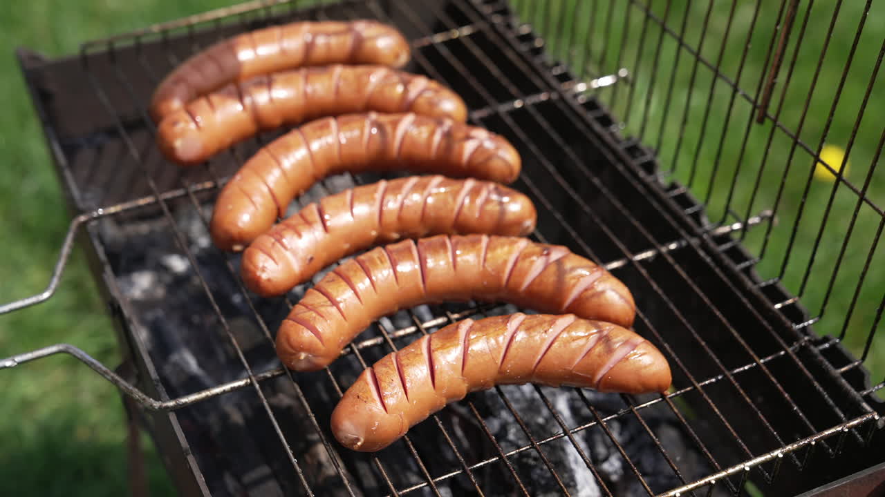 Hot dog sausages roasting in smoke. Chef opens grill grate and turns over juicy sausages. Delicious food for picnic in summer. Eating in nature.