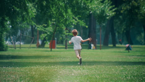 Energetic-elementary-age-boy-run-at-green-lush-field-on-sunny-day.-Camera-zoom.