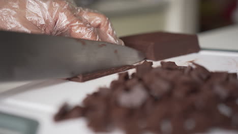 hand in disposable glove chopping dark chocolate bar on cutting board