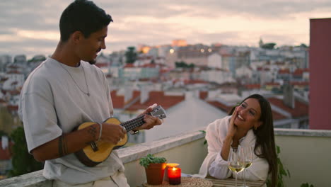 handsome man playing guitar at sunset city view terrace. couple romantic date