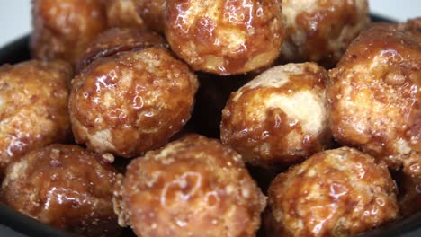 imágenes en bucle de muchas nueces de macadamia confitadas girando en un pequeño cuenco contra un fondo blanco.