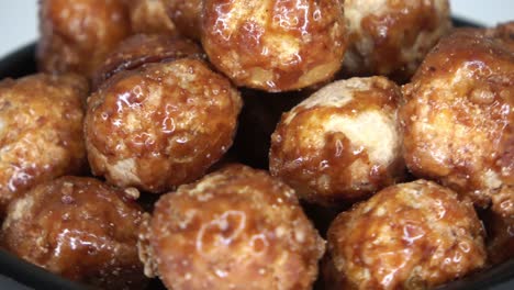 loopable footage of many candied macadamia nuts spinning in a small bowl against white background.