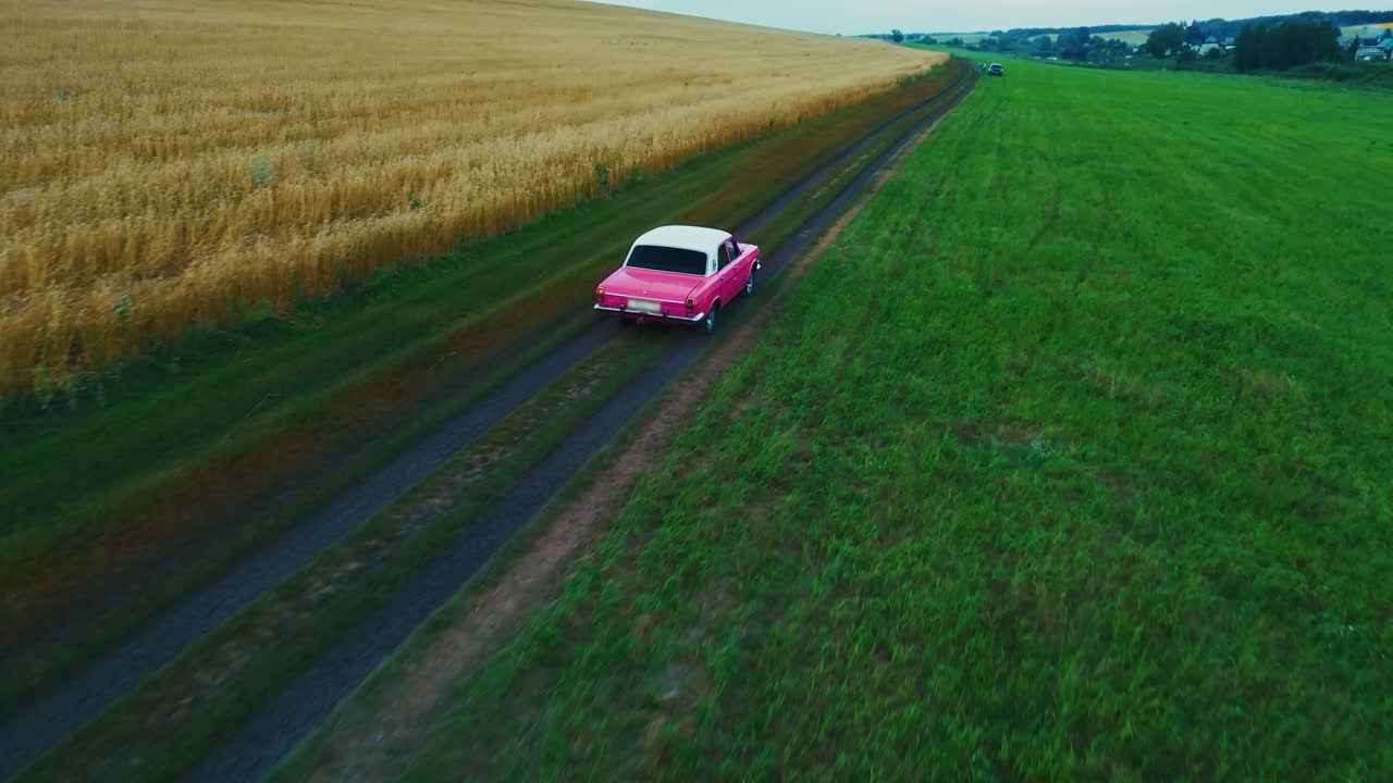 Pink Vintage Car on a Country Road Through Fields