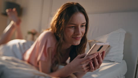 smiling female speaking mobile phone lying bed in morning sunlight close up.