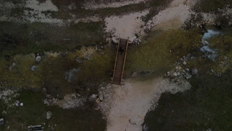 Person-walk-crossing-a-wooden-bridge-over-small-stream-of-water