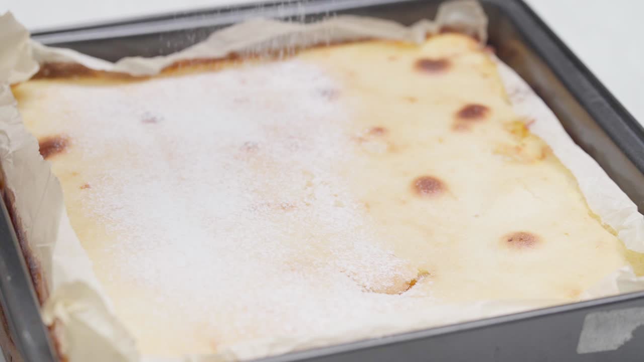 Revet kokos drysses over en nystekt sitronkake i en form, og skaper et mykt og teksturert topping.