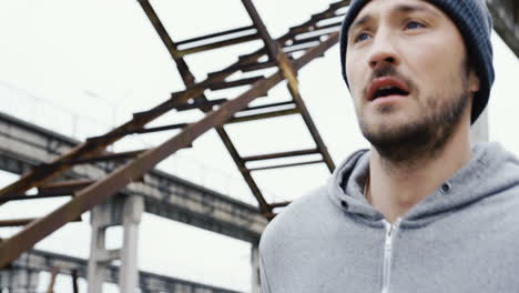 close-up view of a young sportsman in grey hoodie jogging in a old factory ruins on a cloudy morning