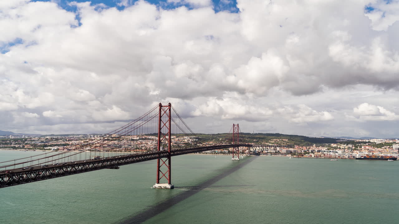 Timelapse della città di Lisbona, Portogallo, Ponte 25 Aprile con nuvole che passano dietro di esso, movimento di veicoli sul ponte che collega la città di Lisbona e imbarcazioni che navigano sul fiume Tago