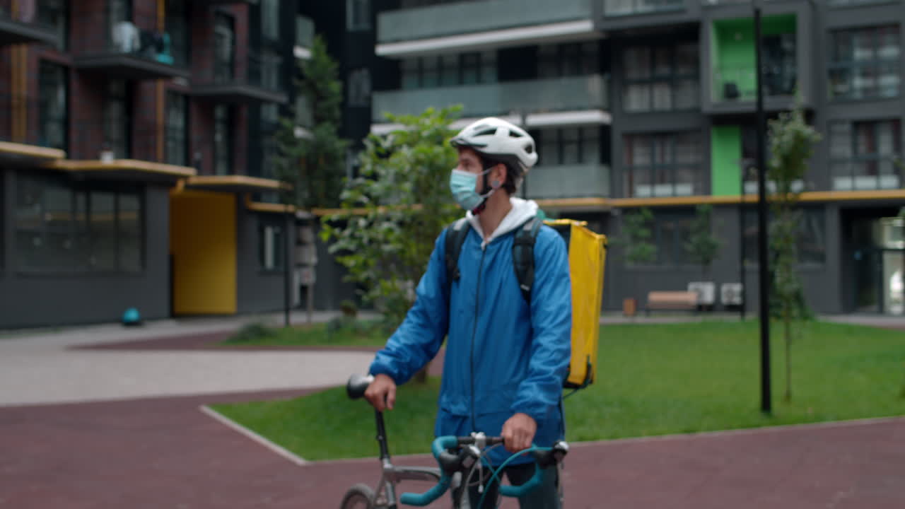 Delivery person with face mask and bicycle helmet in front of a building