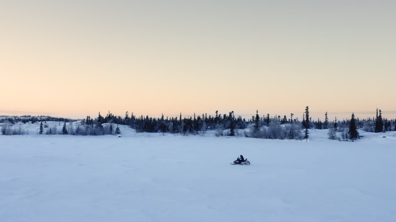 Luftfoto som følger en person som kjører snøscooter på en frossen innsjø om kvelden.