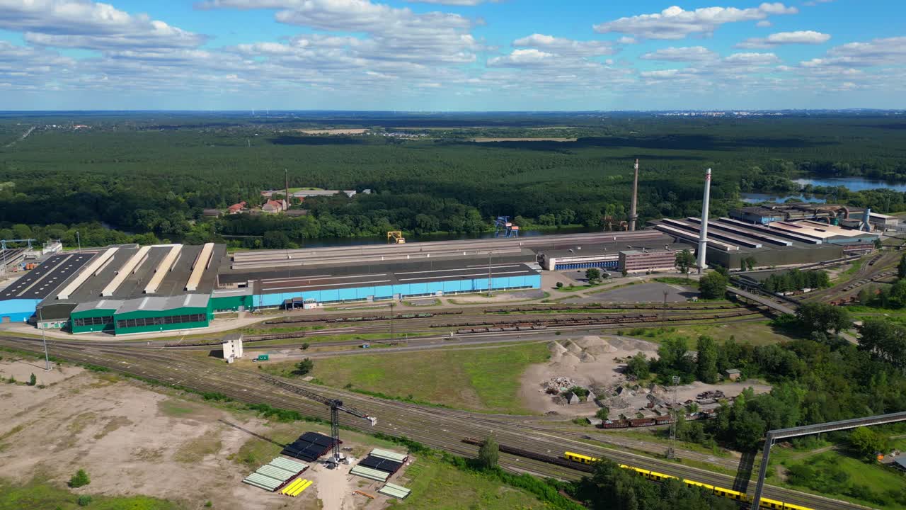 Hennigsdorf steel factory with chimneys, warehouses, railway, near river and forest in summer. Unique aerial view flight panorama overview drone