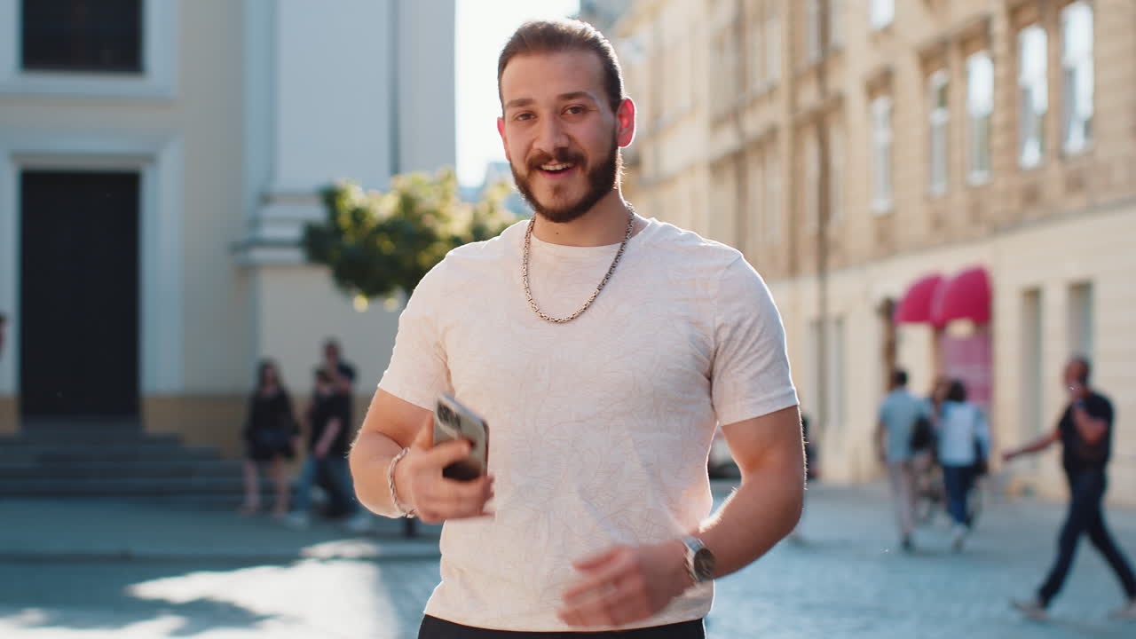 젊은 남자가 스마트폰을 사용하고 문자 메시지를 입력하고 인터넷을 탐색하고 카메라를 보고 일을 마치고 있습니다.