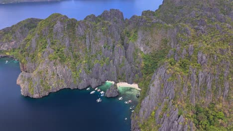 towering limestone cliffs rise above the turquoise waters and white sand of jiji's beach in secret lagoon, miniloc island, philippines, with traditional boats anchored in the calm blue bay