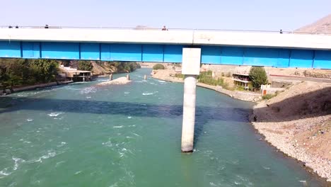 An-aerial-shot-of-a-bridge-crossing-a-river-in-a-village,-with-cars-crossing-the-bridge