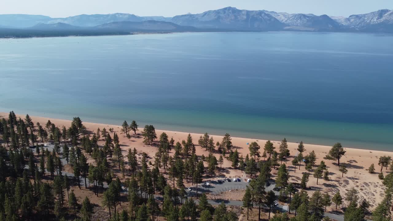 disparo de un dron desde el bosque con vistas a la playa de nevada y al lago tahoe con las montañas de sierra nevada al fondo