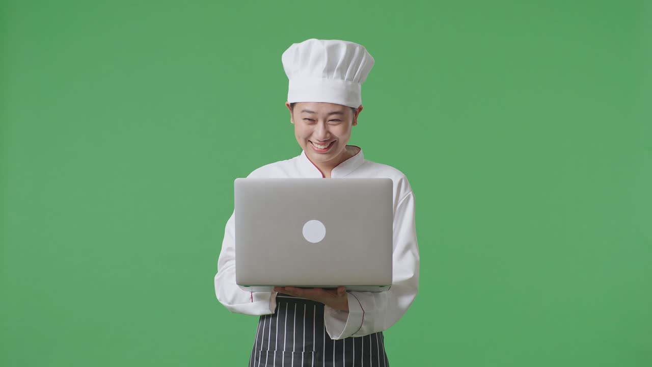Asian Woman Chef Looking At A Laptop Then Screaming Goal Celebrating While Standing In The Green Screen Background Studio
