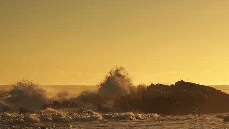 Olas-Del-Mar-Agitadas-Rompiendo-En-Las-Rocas-Creando-Un-Enorme-Rocío-Durante-La-Puesta-De-Sol-Dorada---Toma-Estática-Amplia