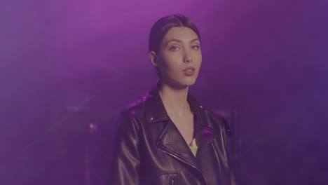 hermosa chica con chaqueta de cuero mirando con confianza a la cámara en la discoteca