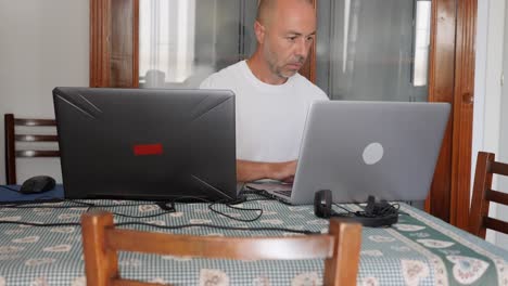 middle-aged bald man working with two laptops at home