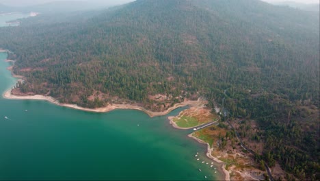 aerial drone flyover lake shore, hazy foothill forests, campgrounds and cabins at bass lake, california