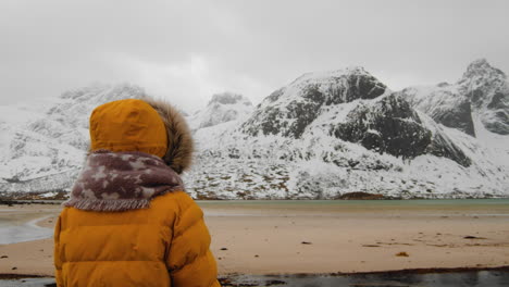 dama con chaqueta acolchada mirando montañas nevadas durante el invierno en la isla de lofoten, noruega