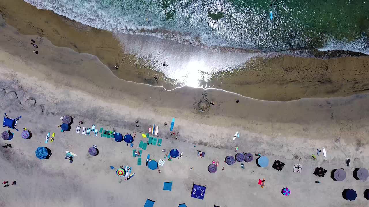 People lounging on white sand beach with umbrellas and chairs with surfers during vacation