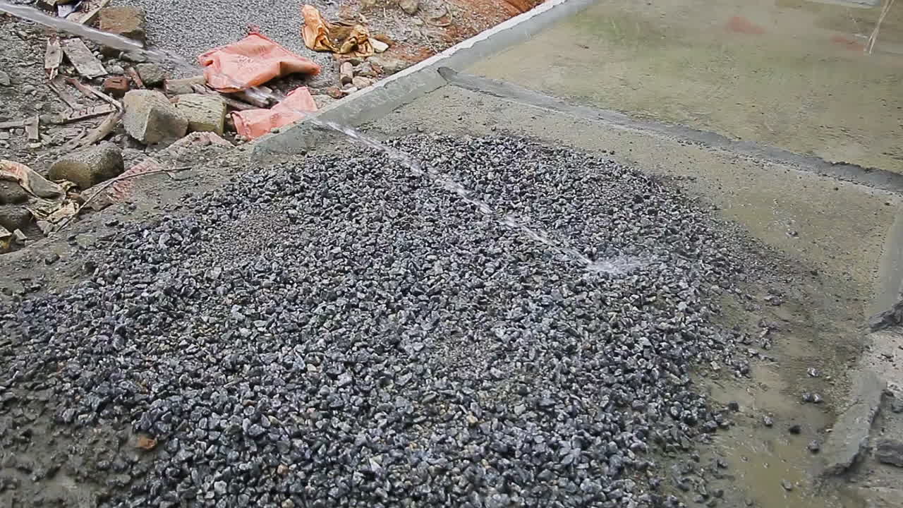 Water is being poured over a mixture of gravel on a construction site by an Indian mason worker, part of an ongoing process