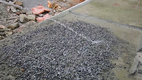 water is being poured over a mixture of gravel on a construction site by an indian mason worker, part of an ongoing process