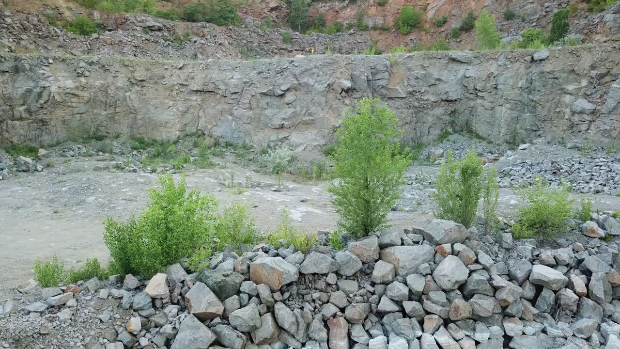 Tourist man with rucksack walking by stone trail over the precipice with mountain lake. Aerial view of a rocky place in summer natural landscape.