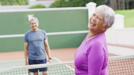 video de una feliz pareja de adultos mayores de dos razas sosteniendo raquetas en la cancha de tenis