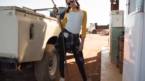 cool biracial woman holding fuel pump standing beside car at petrol station