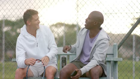 Happy-diverse-male-friends-looking-at-smartphone-and-shaking-hands-at-tennis-court,-slow-motion