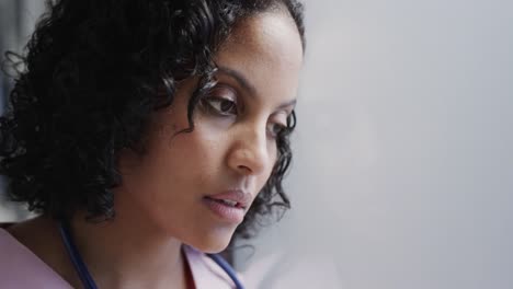 stressed biracial female nurse leaning on wall in hospital in slow motion