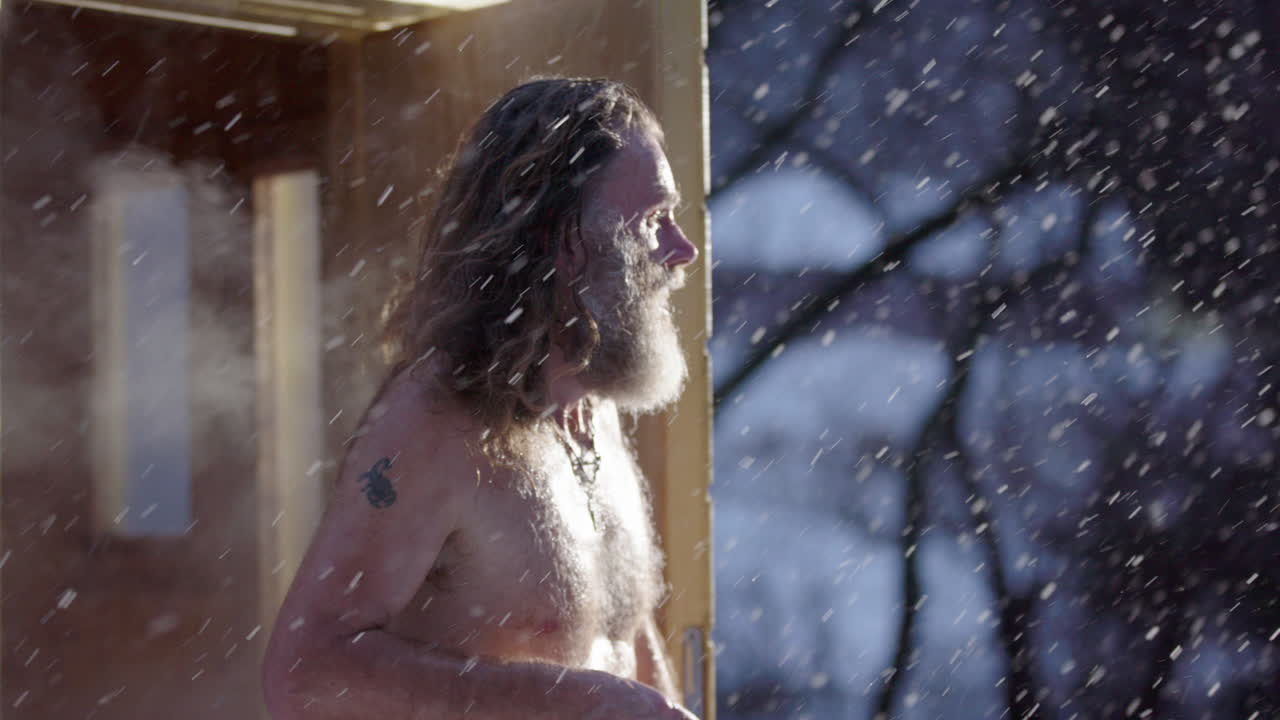Emotional hippy man steps out of hot steaming sauna into snow flurry in winter