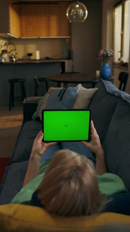 woman using tablet on a couch with a green screen