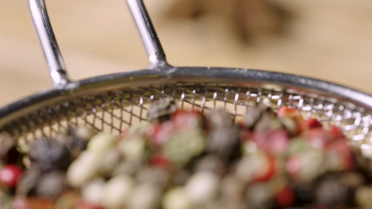 la cámara se centra en una mezcla de granos de pimienta secos de colores. primer plano de granos de pimienta rosada, negra y blanca que se encuentran en un tamiz en la mesa de la cocina. especias y condimentos para cocinar comida picante. cámara lenta