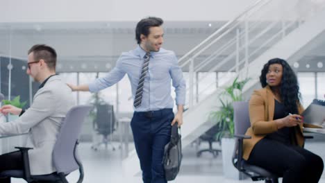 joven hombre de negocios feliz regresa al trabajo después de las vacaciones, entra en una oficina moderna y brillante, saluda a todos, tiene lugar en su computadora de escritorio.