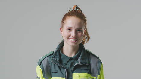 studio portrait of smiling young female paramedic against plain background