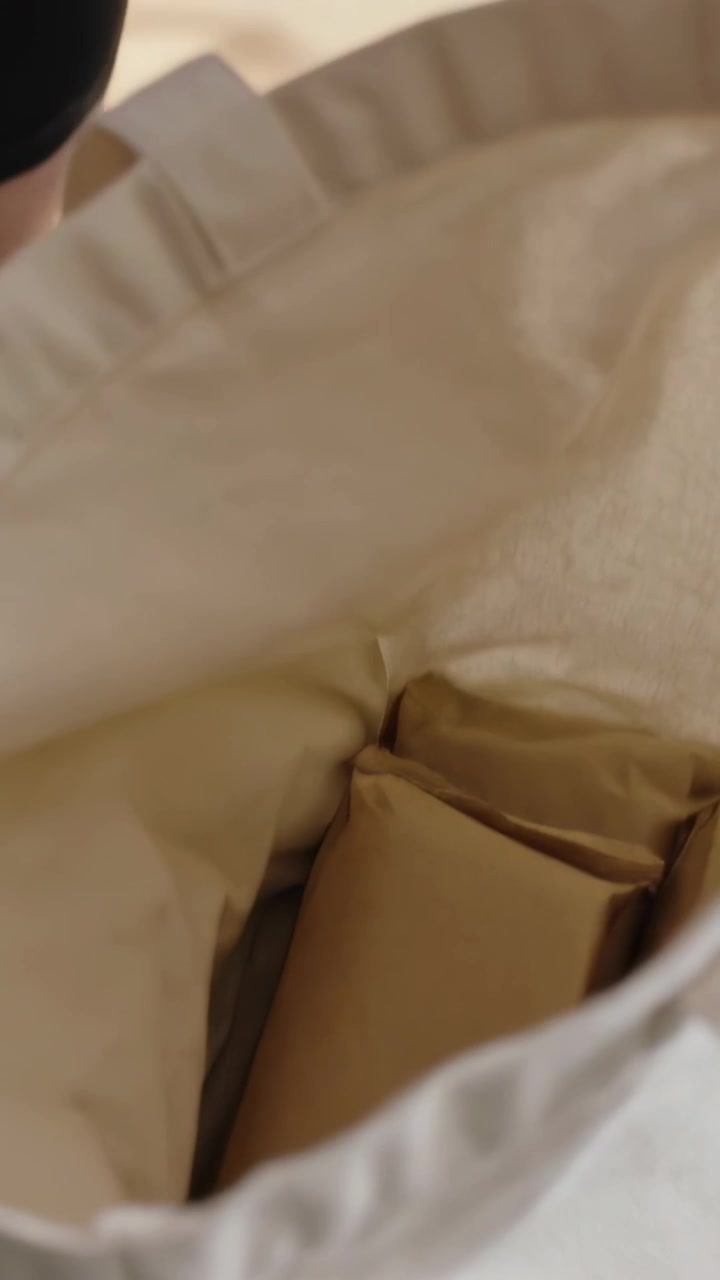 Vertical video: Offering parcel, woman in white tank packing parcels into tote to carry from studio