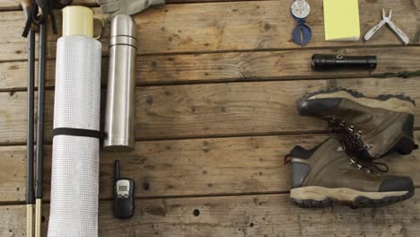 camping equipment with thermos, foil, torch, boots and copy space on wooden background