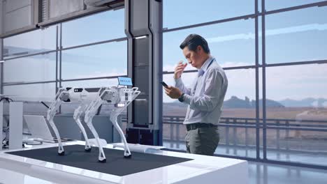 vista lateral completa del cuerpo de un trabajador profesional masculino asiático de pie con su teléfono en una fábrica de alta tecnología, perro robot, está asintiendo con la cabeza con decepción