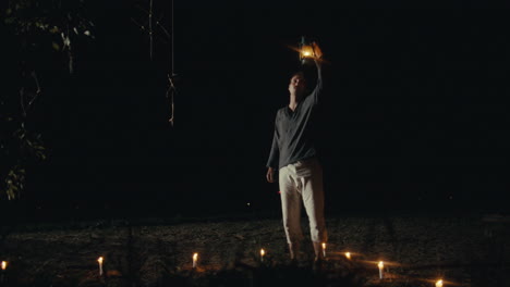 man holding a lantern surrounded by candles at night