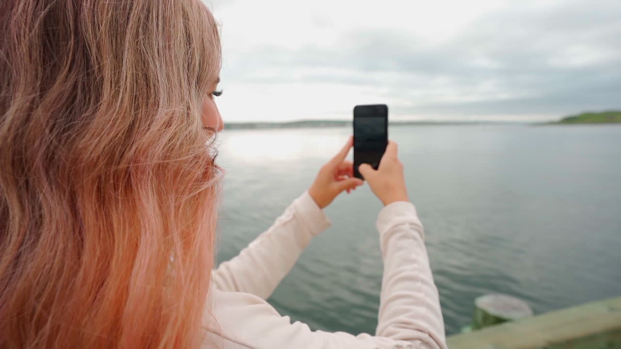 Mulher com cabelo rosa na costa do leste do Canadá tirando uma foto com seu iPhone ao meio-dia